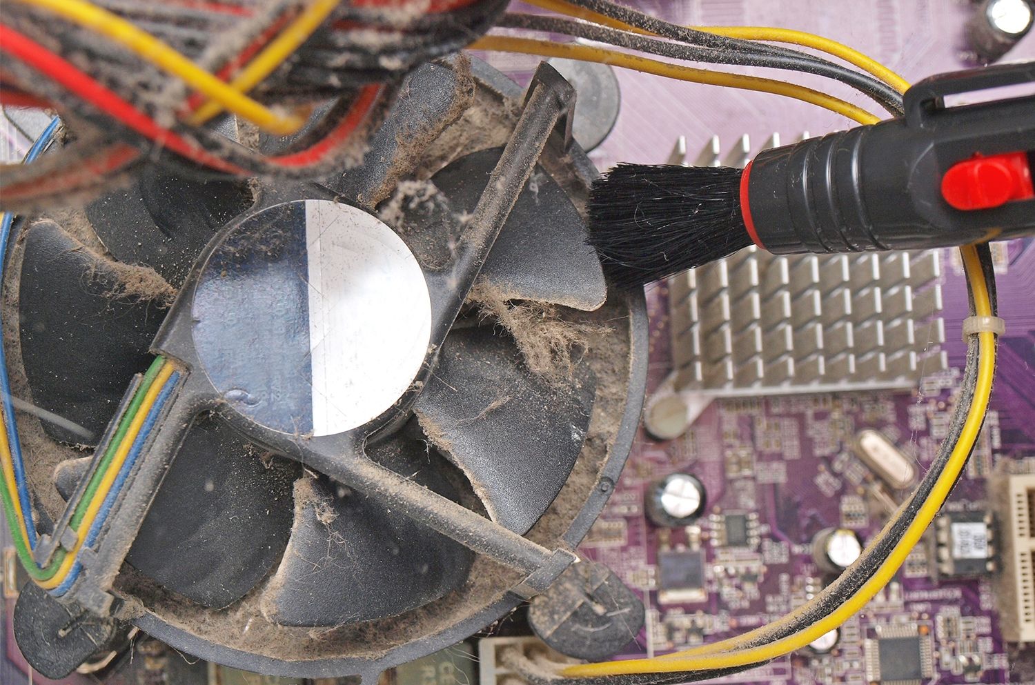 소형 브러시로 데스크톱 컴퓨터의 노출된 팬에서 먼지와 보푸라기를 제거하는 장면